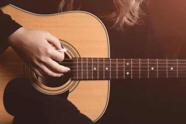 Photo of girl plays an acoustic guitar. close-up of strings