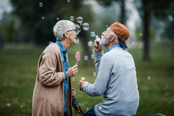 istock Playful senior couple blowing bubbles from bubble wand at the park. 1179772680