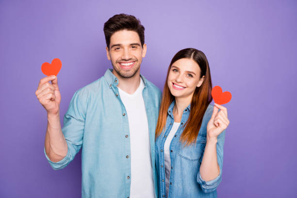 retrato de los cónyuges hermosos románticos tienen regalos de corazones rojos tarjeta de papel para 14-febrero abrazo abrazar usar traje moderno bien guapo aislado sobre fondo violeta púrpura - atuendo con vaqueros para el novio fotografías e imágenes de stock