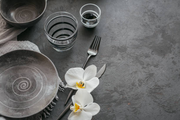 istock Elegance table setting with knitted grey napkin, cutlery, ceramic plates, glasses and white orchid flowers 1179775599