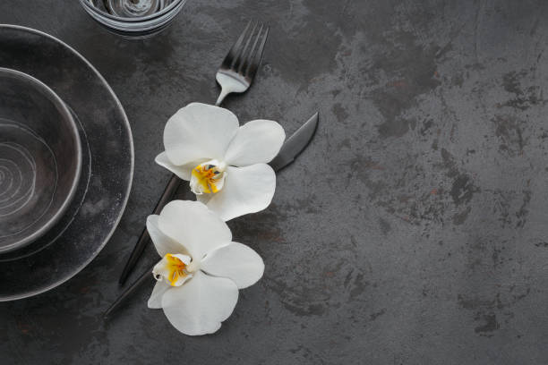 istock Elegance table setting with knitted grey napkin, cutlery, ceramic plates, glasses and white orchid flowers 1179775615