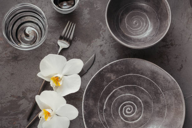 istock Elegance table setting with knitted grey napkin, cutlery, ceramic plates, glasses and white orchid flowers 1179775619