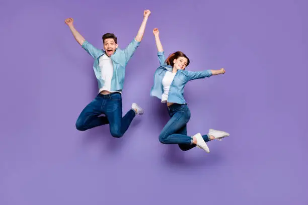 Full body photo of funny funky crazy cheerful married students with brown hair, redhair jump have relax spring holidays date raise hands wear youth clothes isolated over purple color background