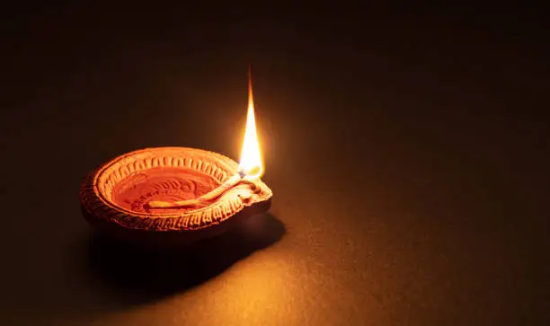 Happy Diwali. Clay diya candle illuminated in Dipavali, Hindu festival of lights. Traditional oil lamp on dark background, copy space.