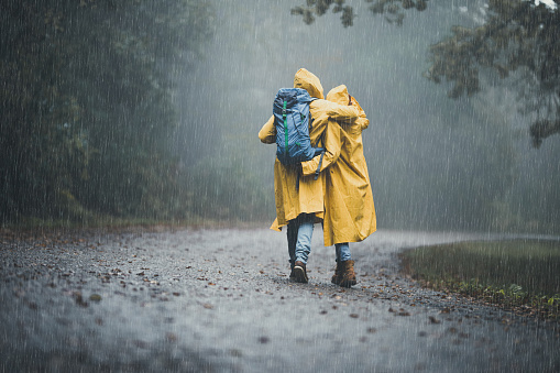 Rear view of loving couple in yellow raincoats hiking through park on a rainy day. Copy space.