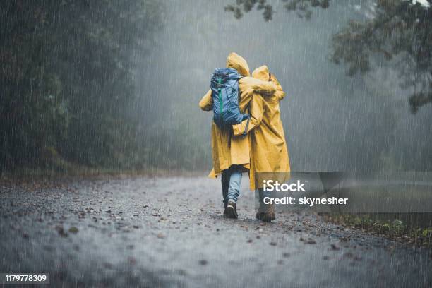 Back View Of Embraced Couple In Raincoats Hiking On A Rain Stock Photo - Download Image Now