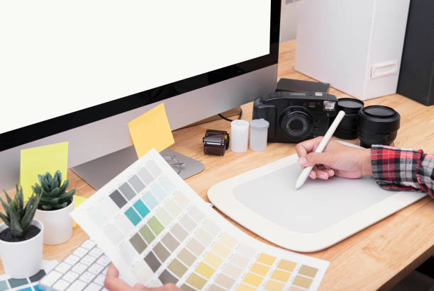 istock Graphic designer artist using graphics tablet drawing and looking at colour chart his work at desk in office. 1179780001