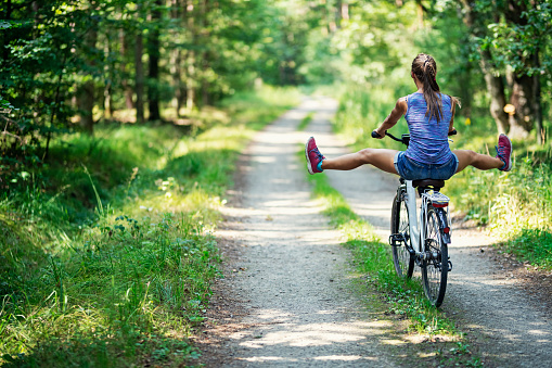 Happy teenage girl enjoying a bike ride through the forest.\nNikon D850