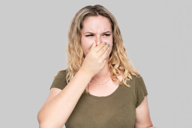 Girl covers nose with hand showing that something stinks isolated on gray background stock photo