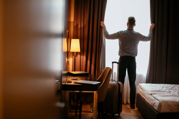 uomo d'affari che guarda attraverso la finestra della camera d'albergo - laptop adult curtain business foto e immagini stock