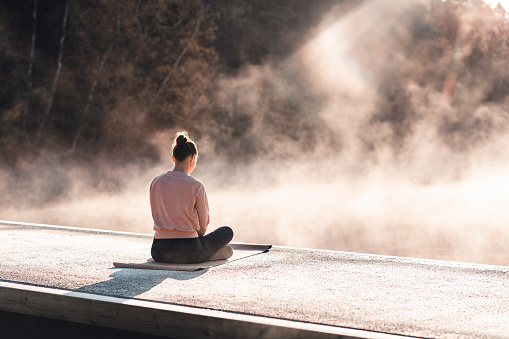A young woman is exercising yoga by a lake early in the morning on a beautiful autumn day.