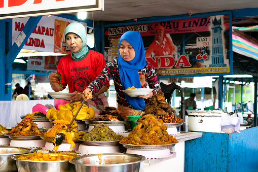 Bukittinggi, West Sumatra, Indonesia - February 2019. People taking a lunch in culinary restaurant in a Pasar ateh, smallt. Nasi Kapau is a Minang steamed rice topped with various choices of dishes originated from Nagari Kapau, Bukittinggi, a tourism and culinary hotspot town in West Sumatra, Indonesia