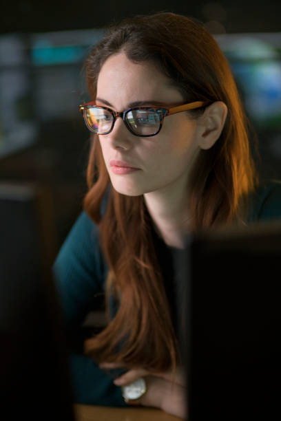 Computer Alert Stock photo of a good looking professional woman contemplating the content of a computer display in a dark office. eye reflection stock pictures, royalty-free photos & images