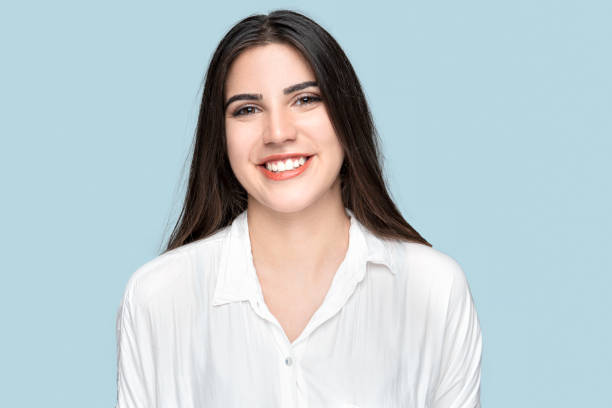 Young long-haired smiling woman in white shirt over blue background stock photo
