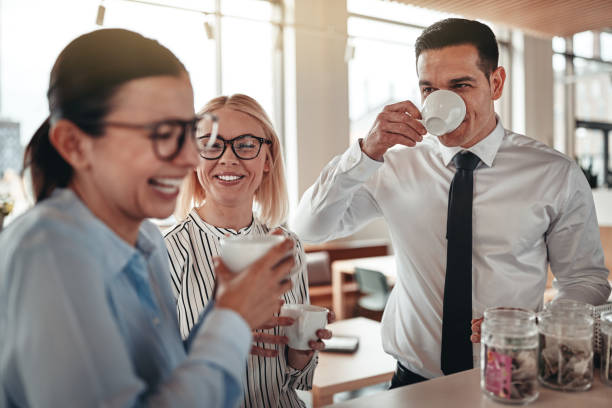 Young businesspeople laughing together during their office coffee break Group of young businesspeople laughing together during their coffee break in a bright modern office coffee break stock pictures, royalty-free photos & images