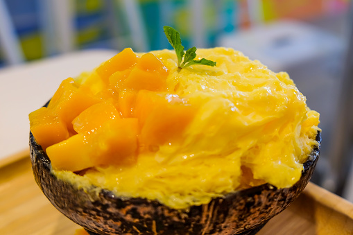 Close up delicious mango shave iced with sliced of mango fruit inside coconut bowl