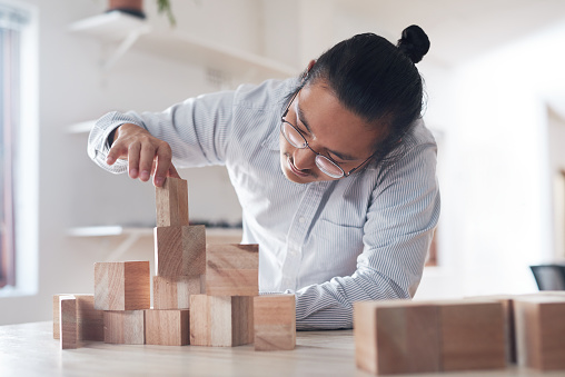 Shot of a young businessman working with wooden building blocks in a modern office