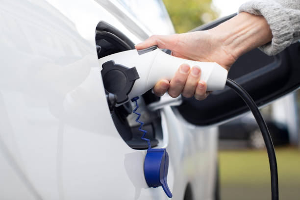 feche acima da mão que une o cabo de alimentação ao carro elétrico de emissão zero ambientalmente amigável - electric plug electricity power cable - fotografias e filmes do acervo