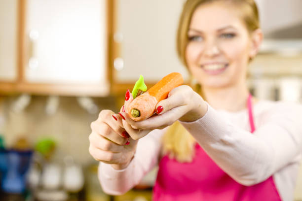 Woman peeling vegetables using food peeler. Cooking female preparing carrot before serving.