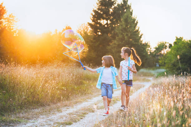 Happy little friends playing with soap bubbles in a field.