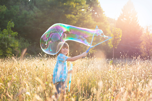Happy child playing with soap bubble in a field.