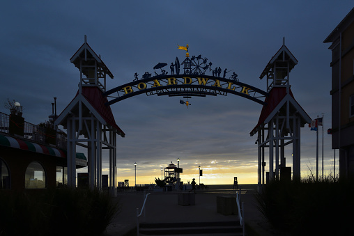 Ocean City, Maryland, boardwalk entrance at sunrise.  There is a jogging woman silhouetted in the center background, otherwise just the surrounding tourist stops and equipment