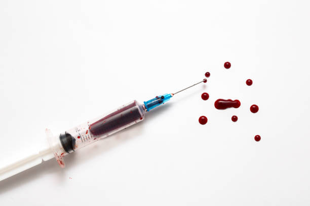 Closeup of a disposable syringe and many blood drops isolated on white stock photo