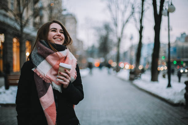 Happy young woman wearing warm clothing walking on street during winter stock photo
