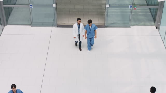 Overhead view looking down on medical professionals walking through hospital lobby with patients having discussion - shot in slow motion