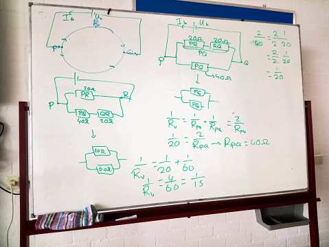 Part of a class room with standing white board. Diagrams and calculations are written on the white board.