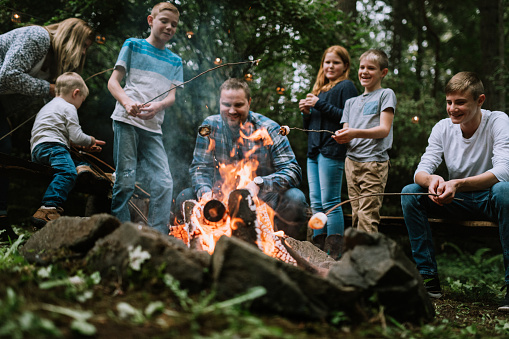 A young family enjoys relaxing by a fire, roasting marshmallows for S'mores. A time of bonding and connection for a loving family.