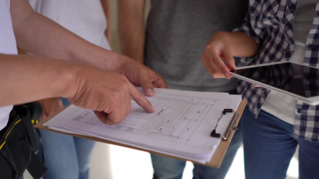 Close up of unrecognizable couple and building contractors holding a tablet and clipboard and closing a deal