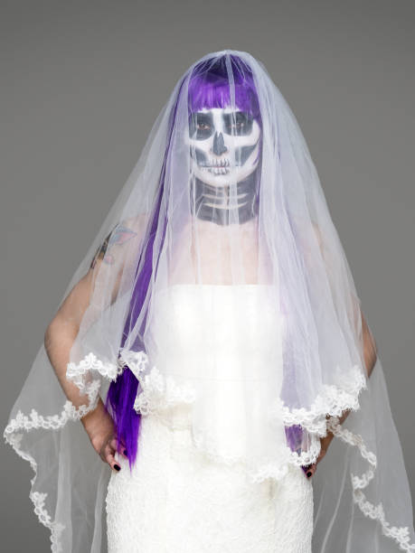 무서운 할로윈 해골 메이크업과 보라색 가발 신부 베일, 회색 배경 위에 웨딩 드레스와 함께 카메라를 보면 여자의 초상화. 블랙 웨딩 - day of the dead mexico bride human skeleton 뉴스 사진 이미지