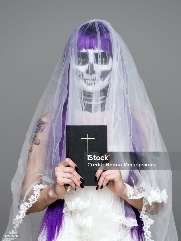 Retrato De La Mujer Mira A La Cámara Con Terrorífico Maquillaje Esqueleto Halloween Y Velo Nupcial Peluca Púrpura Vestido De Novia Sostiene La Santa Biblia Sobre El Fondo Gris Boda Negra Foto Retrato De La Mujer Mira A La Cámara Con Terrorífico Maquillaje Esqueleto Halloween Y Velo Nupcial Peluca Púrpura Vestido De Novia Sostiene La Santa Biblia Sobre El Fondo Gris Boda Negra Foto