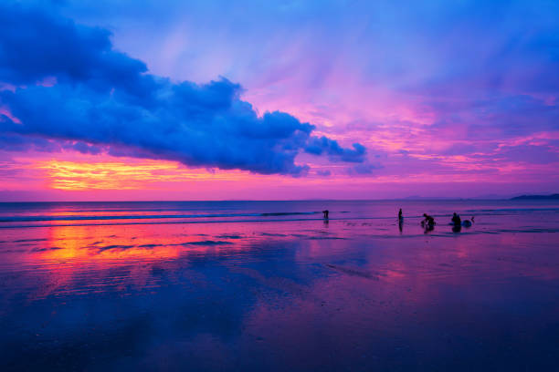 Asian family unloading their catch on the beach at dusk, dramatic clouds and sunset sky in the backgrounds.
