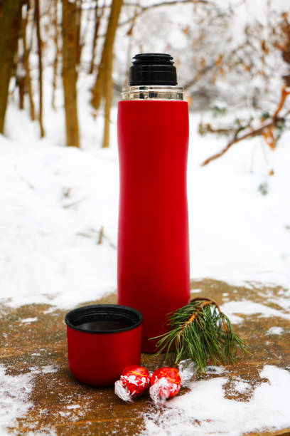 istock Red thermos with sweets on the winter background, open mug , refreshment during hiking in the forest, closeup photo 1179842582