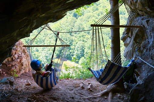 Woman at Suncuius via ferrata, resting in a hammock located in a small cave on the route, with beautiful views of the Crisul Repede defile below, on a bright and hot sunny day.