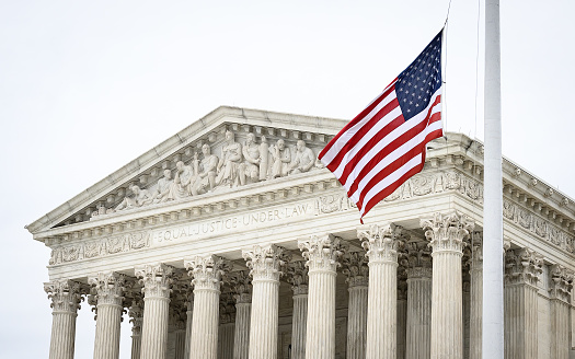 A picture of the supreme court, with the US flag waving in front of the phrase \