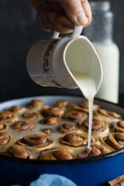 istock Baker putting sugar glaze syrup on to baked cinnamon buns 1179852320