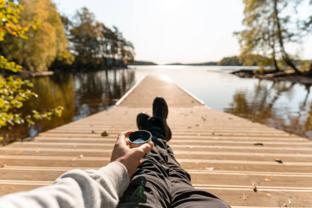 A man is drinking coffee from a thermos out by a lake, seen from his point of view.