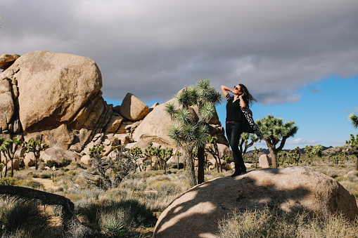 Young traveler woman, wearing vintage boho clothing, enjoying freedom and the beautiful nature in the Joshua Tree parts of the Mojave desert.