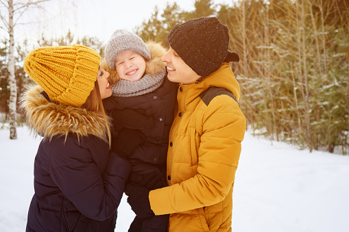 Portrait of happy family in winter day. Mom and dad are cuddling and kissing their little son in winter park. Family lovely moments, copy space