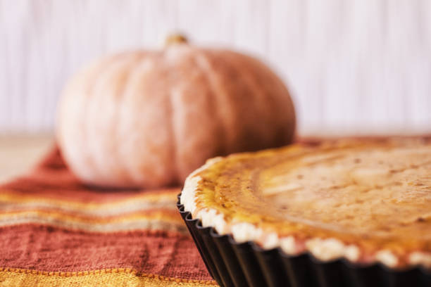 Fresh made pumpkin pie in pie mold at table with whole pumpkin in background, close-up, selective focus
