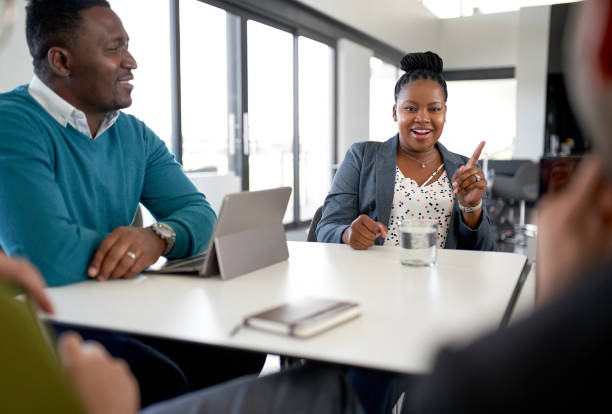 Candid shot of African American female boss meeting with multi-ethnic team of professional colleague businesspeople Unposed shot of black professional female talking with team of diverse mixed race businesspeople in large modern office working on collaboration and teamwork strategies womens issues stock pictures, royalty-free photos & images