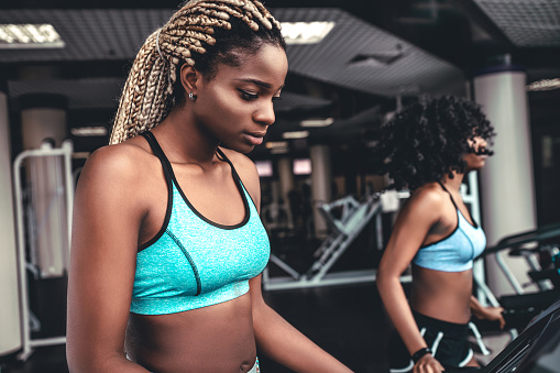 Side view of two attractive athletic women on running track. Black girls on treadmill. Concept healthy lifestyle