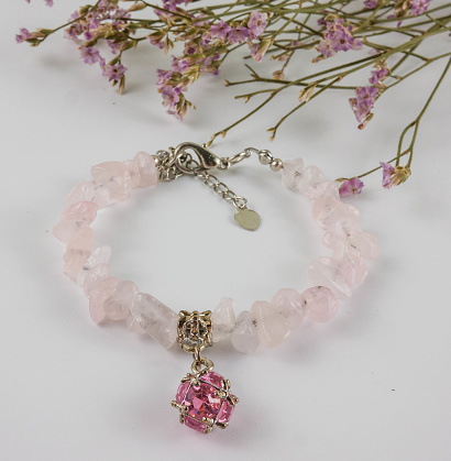 Rose quartz bracelet on white background and dried flower bouquet