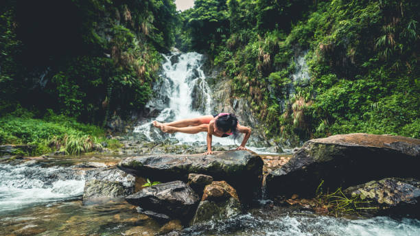 junge frau praktiziert yoga in der nähe von wasserfall im wald - waterfall water nature zen like stock-fotos und bilder