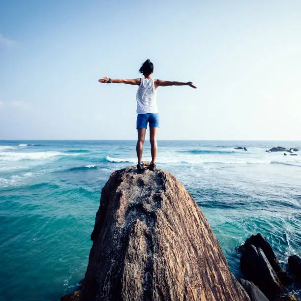 Photo of Freedom young woman outstretched arms on seaside rock cliff edge