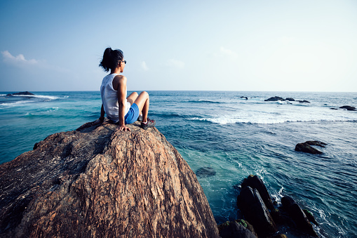 Young woman sit on seaside rock cliff edge thinking