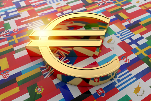 Gold EURO sign with a bright flash on a surface covered with national flags of the EU countries. 3D rendering, illustration.